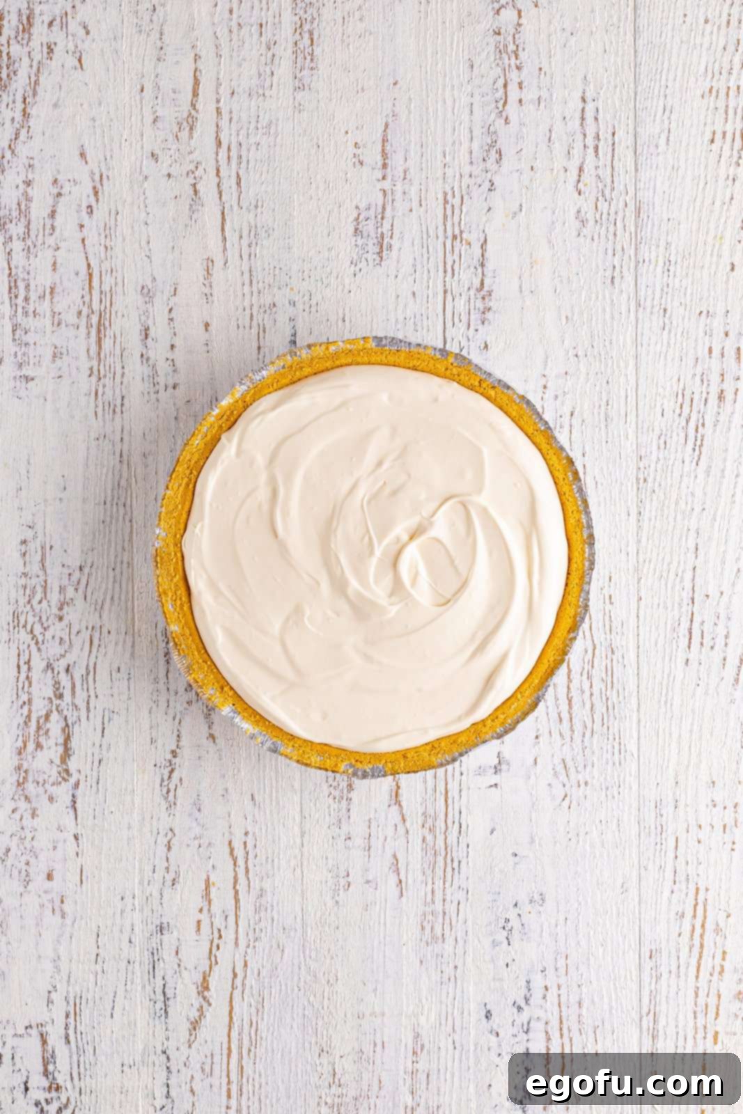 A freshly made lemonade pie, poured into a graham cracker crust and topped with a swirl of whipped cream.