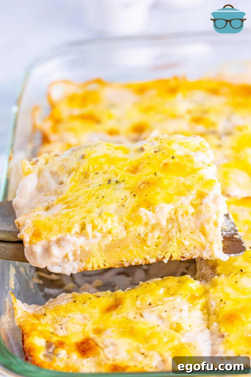 A serving utensil holding some biscuits and gravy casserole, showcasing layers of biscuit, egg, gravy, and cheese.