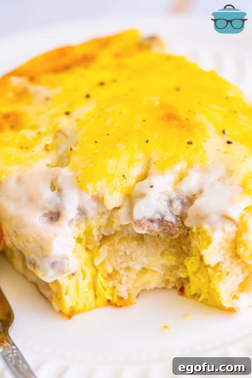 A serving piece of a Biscuits and Gravy casserole with a bite taken out, showing the layers.