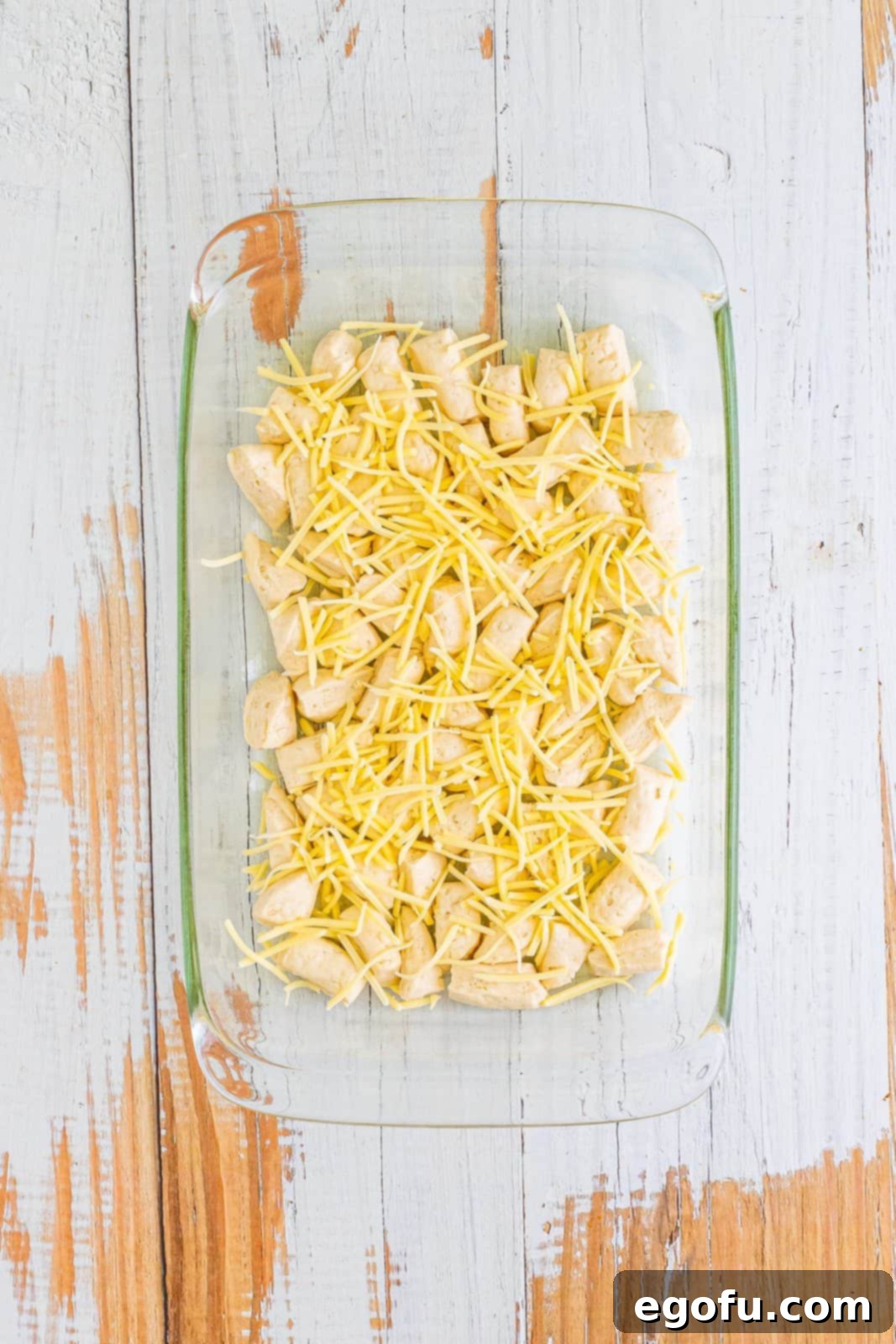 A baking dish filled with biscuit dough pieces and half of the shredded white cheddar cheese.