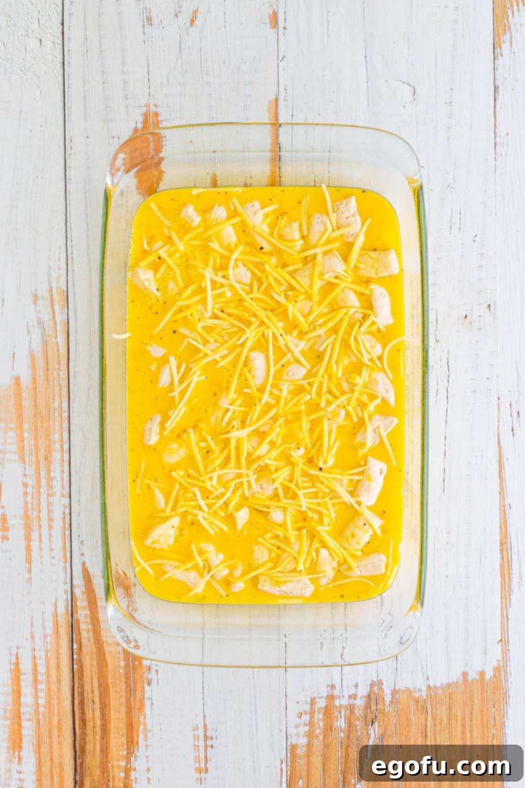 A baking dish with cut up biscuits, cheese, and the egg mixture poured over.