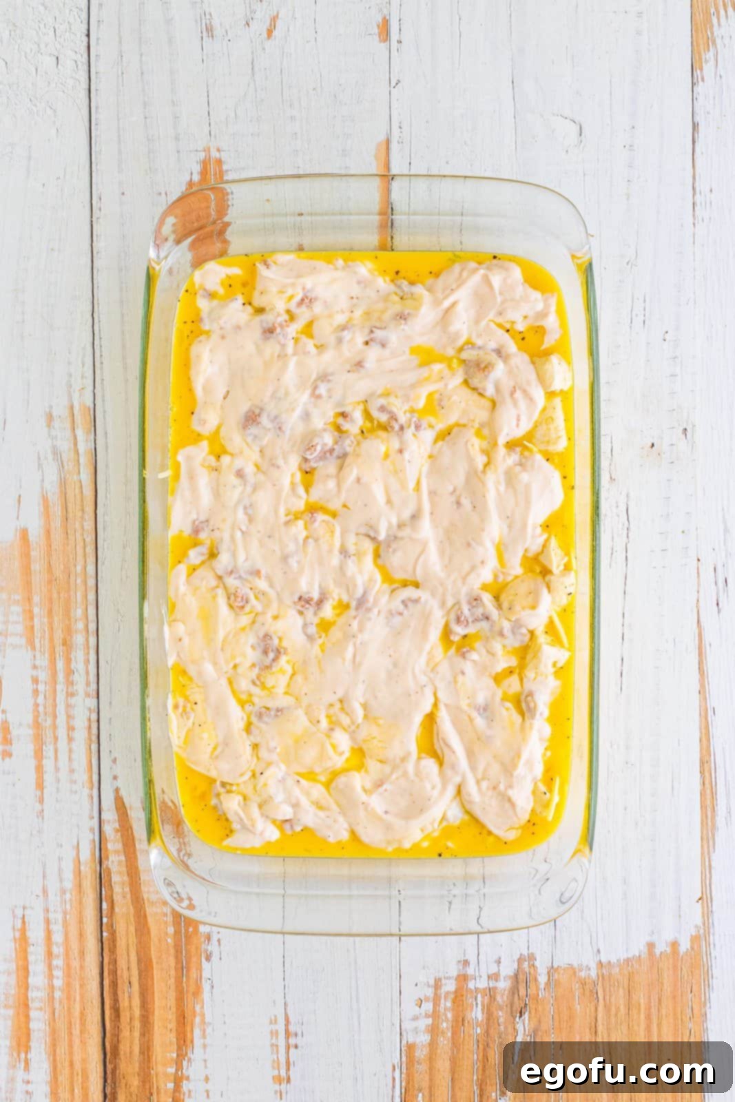 Sausage gravy smoothed over the top of the baking dish containing biscuit dough, eggs, and cheese.