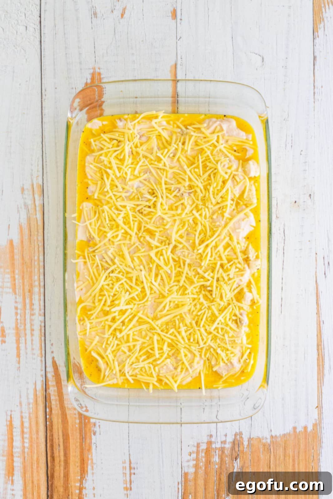 The remaining cheese sprinkled on top of the sausage gravy, biscuits, and eggs in the baking dish.