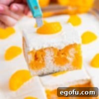 A piece of Orange Creamsicle Poke cake being held over the baking dish with the rest of the cake.