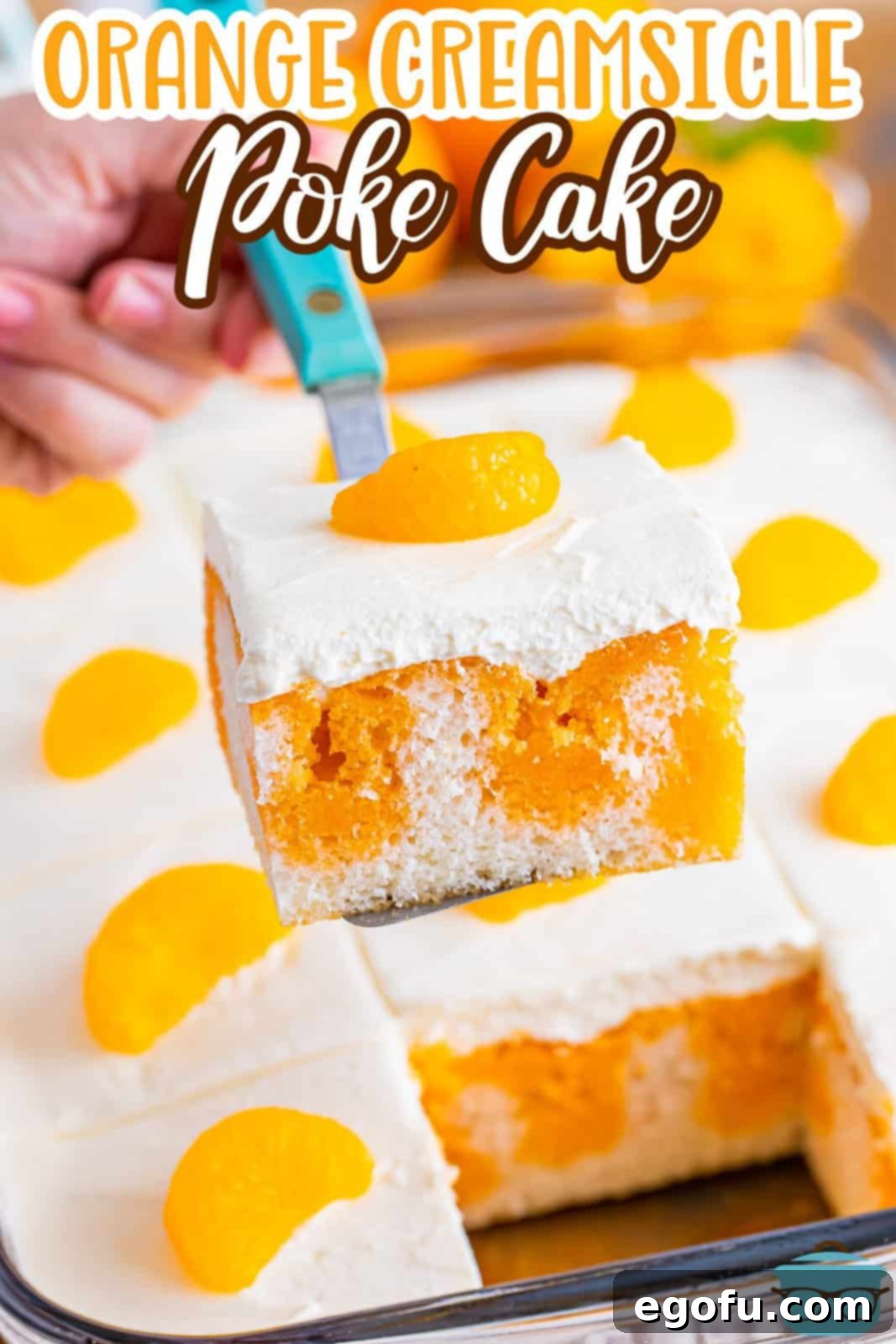 A serving utensil holding a slice of Orange Creamsicle Poke Cake.
