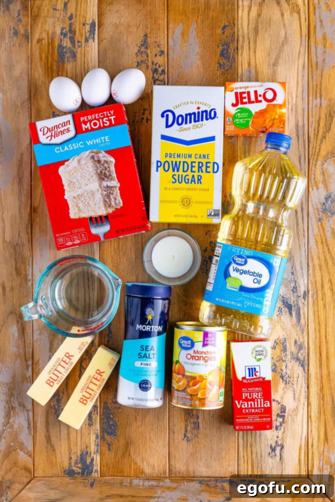 White cake mix, egg whites, oil, water, orange Jell-O, unsalted butter, powdered sugar, milk, vanilla extract, salt, and mandarin orange slices.