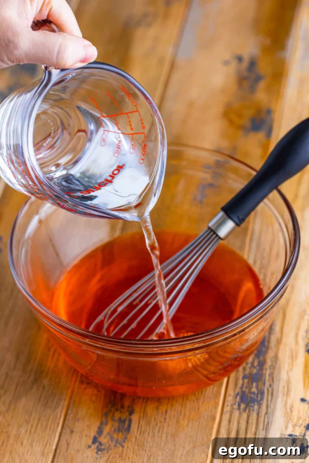 Water being poured into a mixing bowl of Orange Jello powder. 