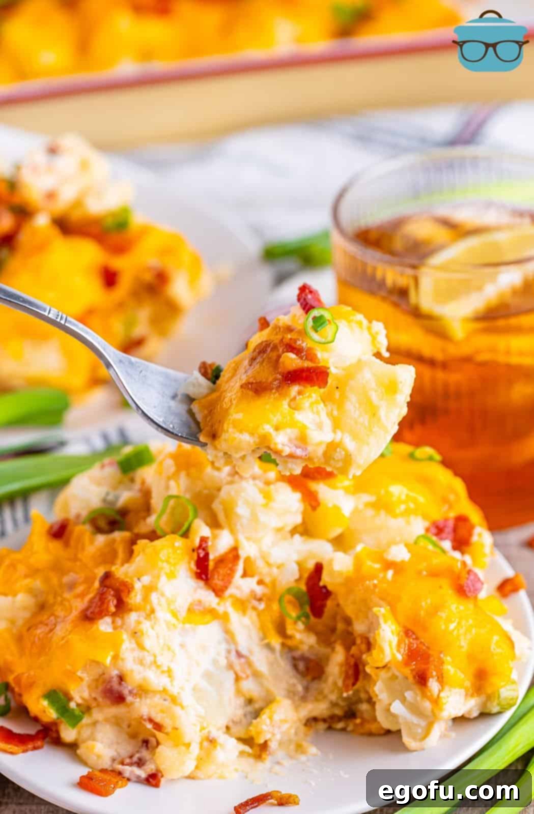 A fork holding a perfect bite of creamy, cheesy, and bacon-filled Twice Baked Potato Casserole, with a full serving dish in the background.