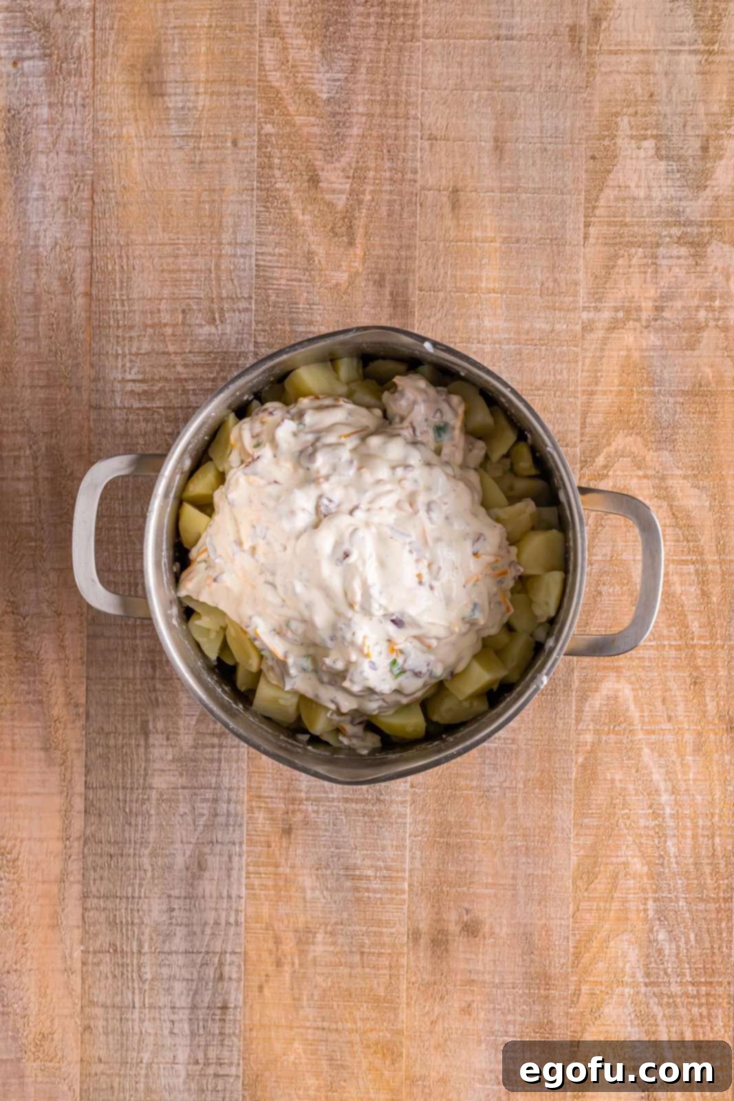 A large pot where the creamy, cheesy mixture has been added to the boiled potatoes, ready to be combined into a delicious casserole base.