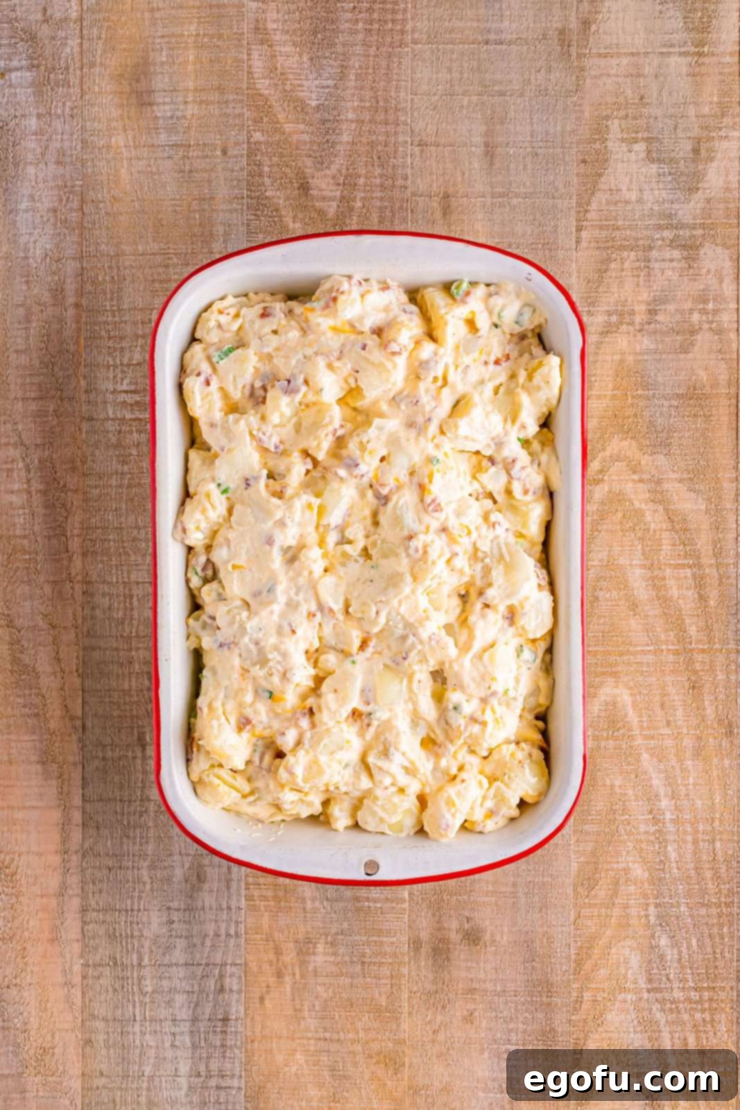 A 9x13-inch baking dish filled with the prepared Twice Baked Potato Casserole mixture, with a layer of shredded cheese awaiting its turn in the oven.
