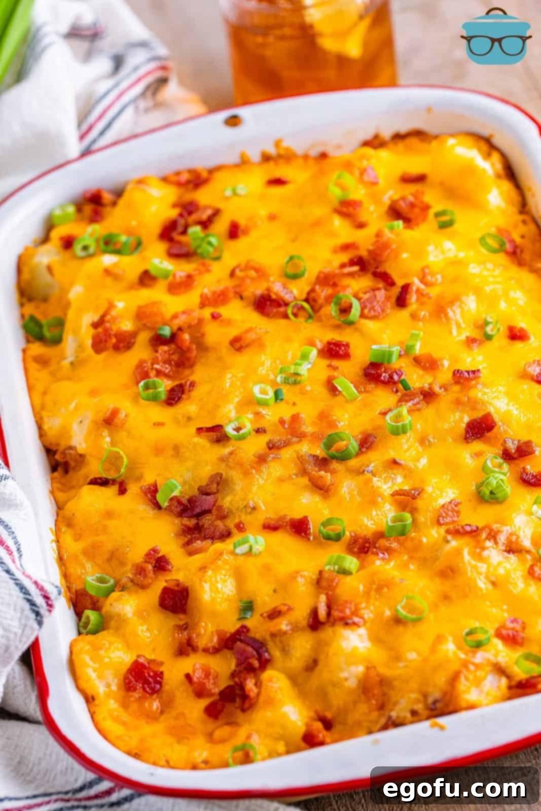 A large baking dish brimming with a finished Twice Baked Potato Casserole, garnished with fresh green onions and crispy bacon bits, with melted, golden-brown cheese.