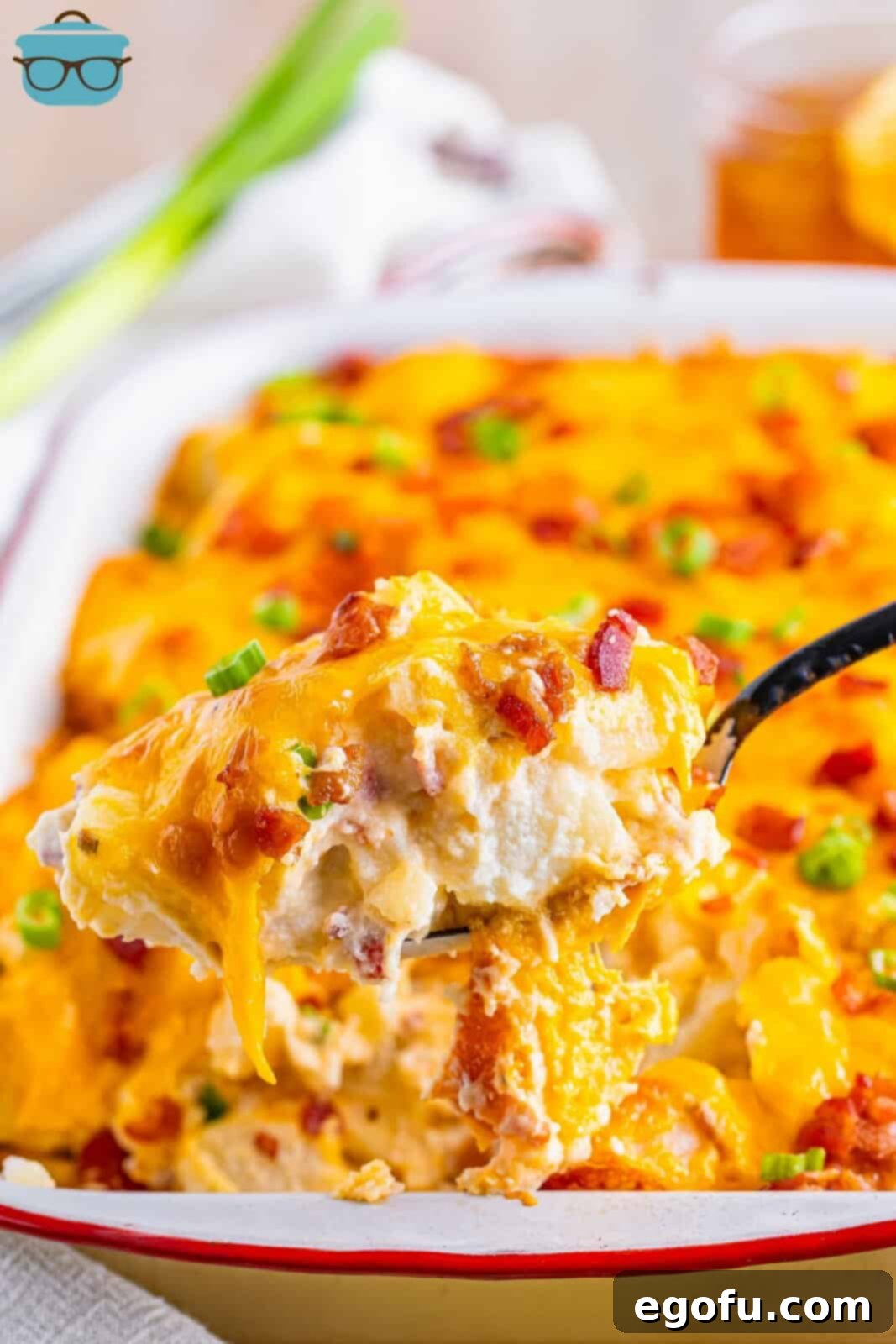 A final inviting image of a bite of the creamy, cheesy Twice Baked Potato Casserole on a fork, poised in front of the full, golden-brown casserole dish.