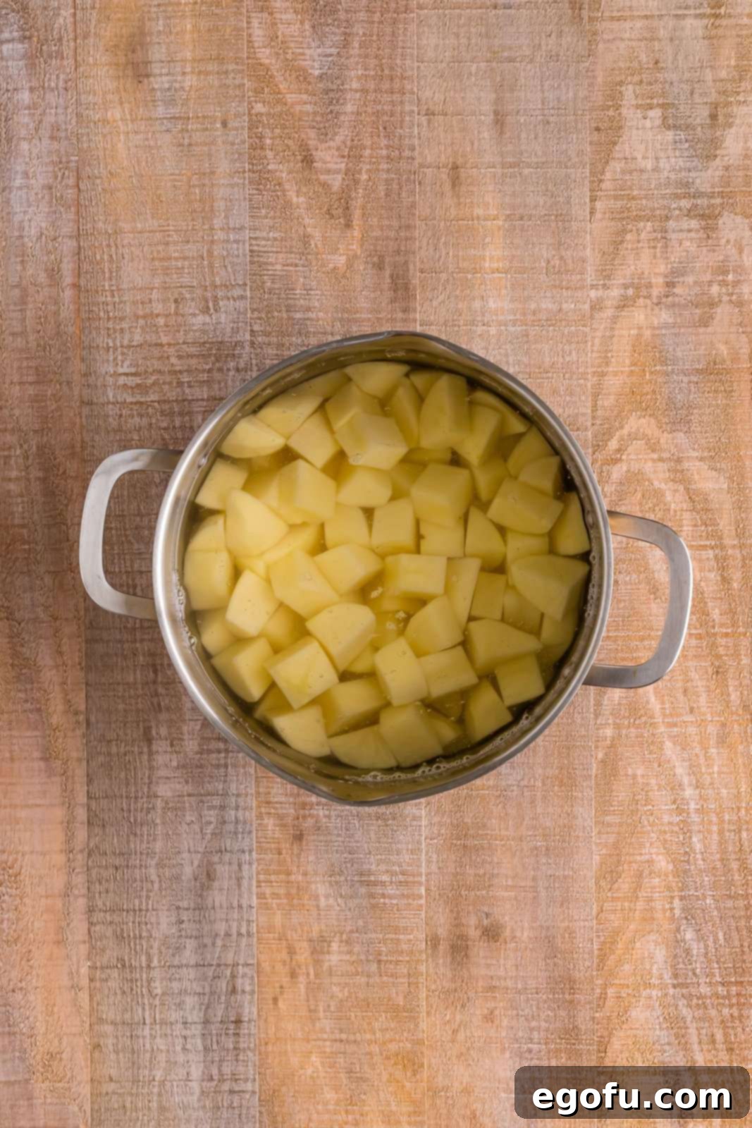 A large stockpot filled with peeled and diced potatoes, covered with cold water, ready to be boiled on a stovetop.
