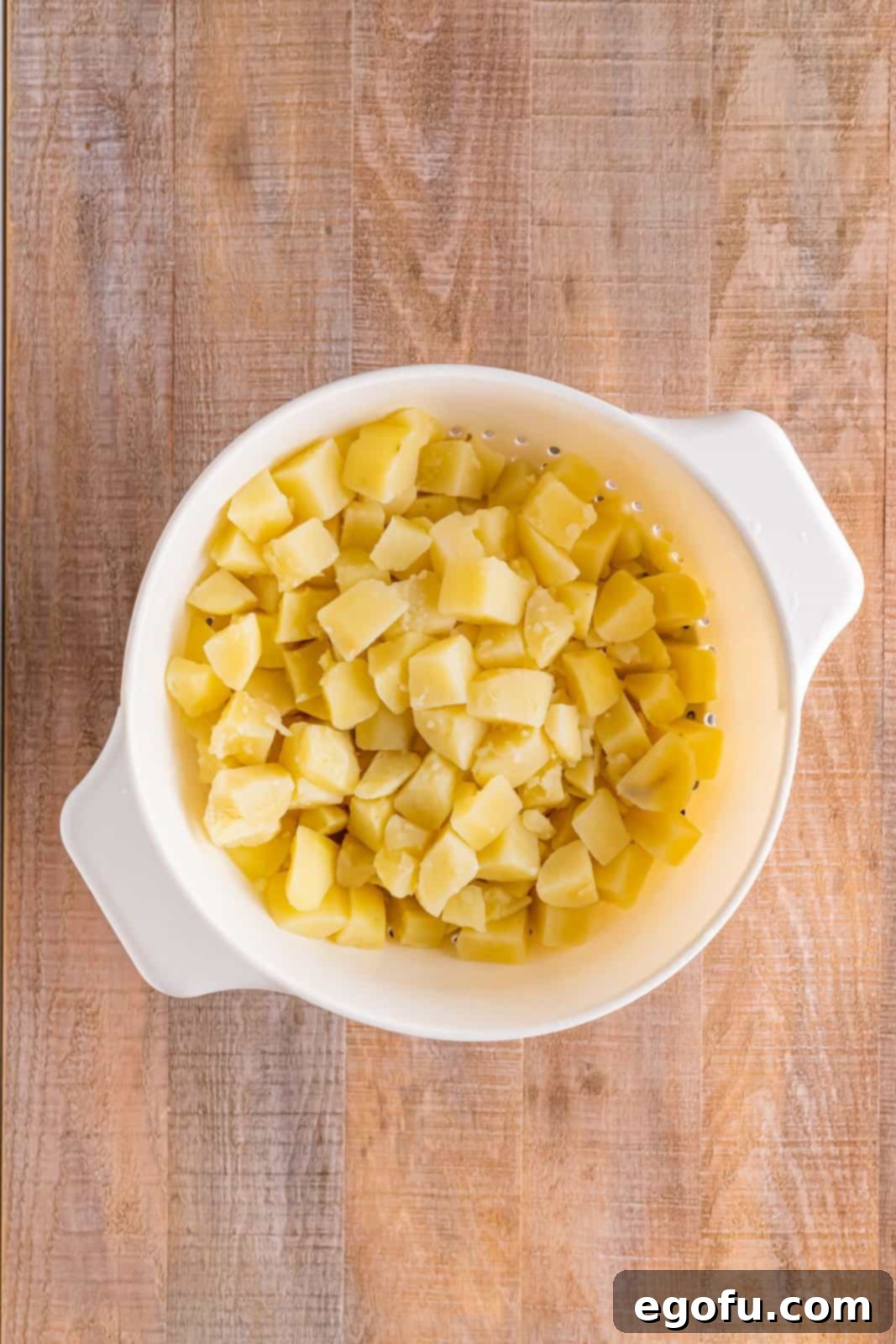 A colander filled with freshly boiled and drained potatoes, steaming gently, after being removed from the pot.