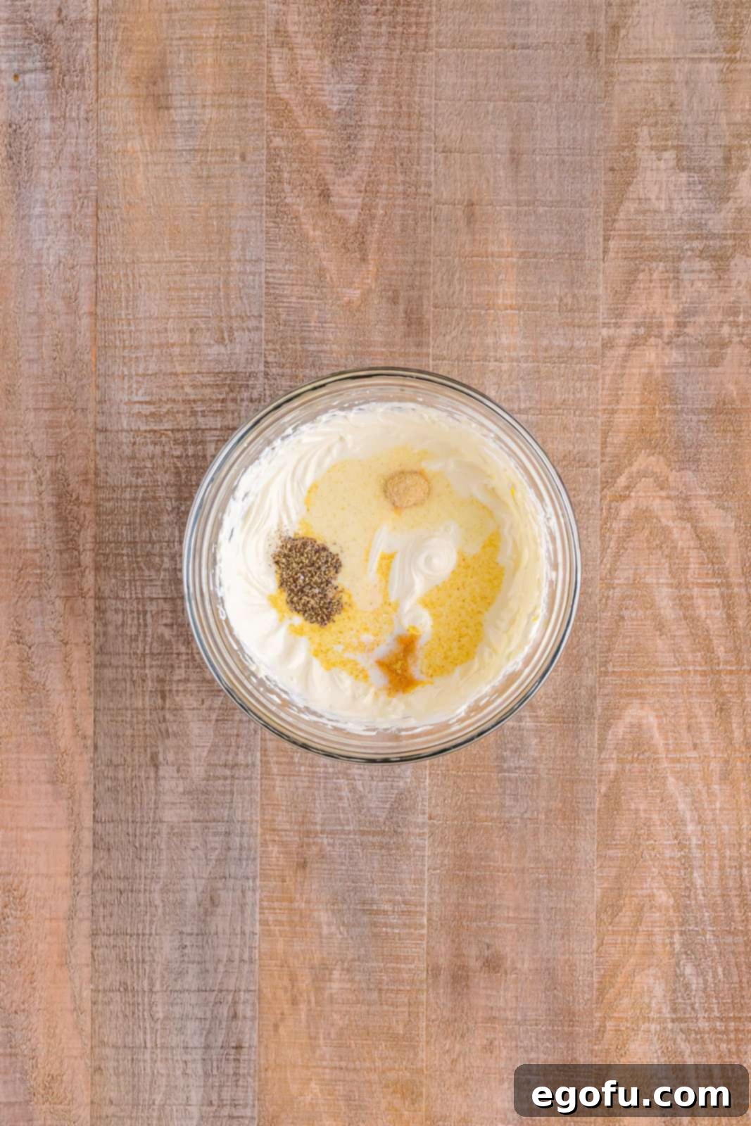 A bowl showcasing the creamy mixture of sour cream and cream cheese, now enhanced with milk and a generous sprinkle of garlic powder, salt, onion powder, and black pepper.