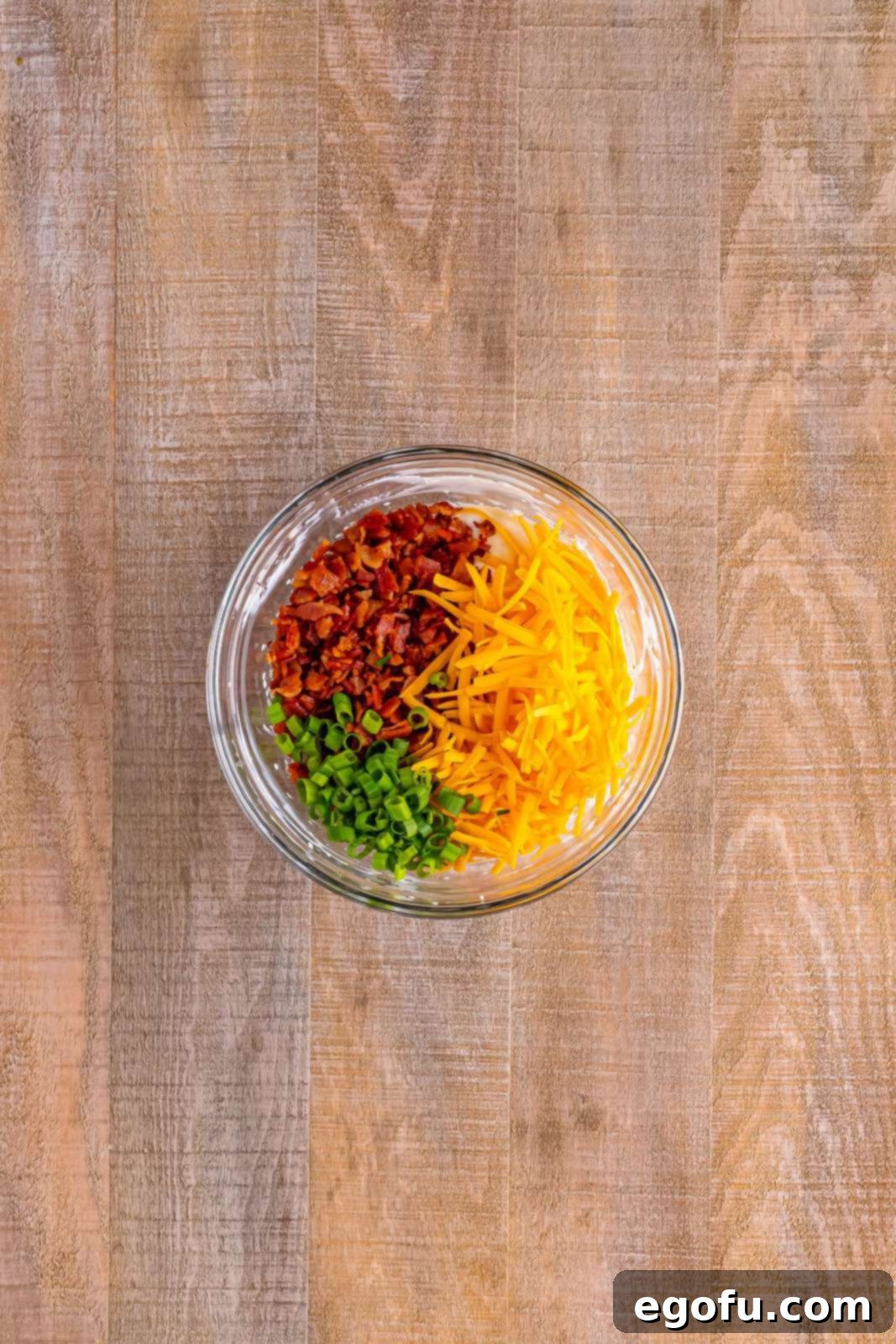 The mixing bowl now contains the creamy cheese and spice mixture, beautifully folded with crispy bacon, vibrant green onions, and shredded cheddar cheese.