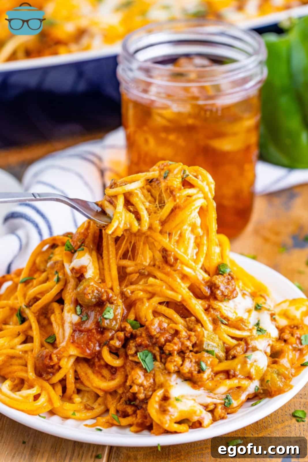 A fork holding a bite of Mexican million dollar spaghetti over a plate of spaghetti.