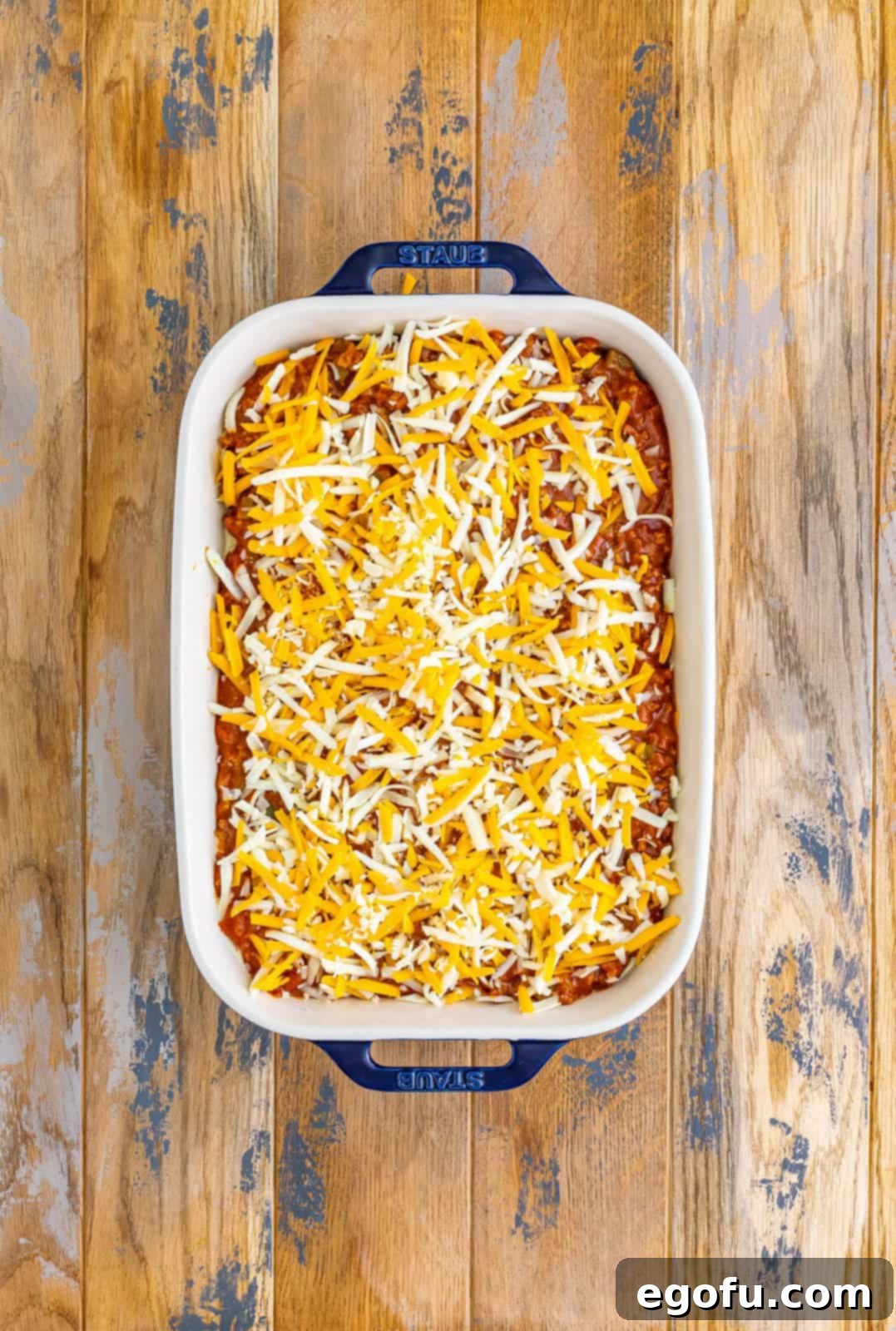 Shredded cheese on top of meat sauce and pasta in a baking dish.