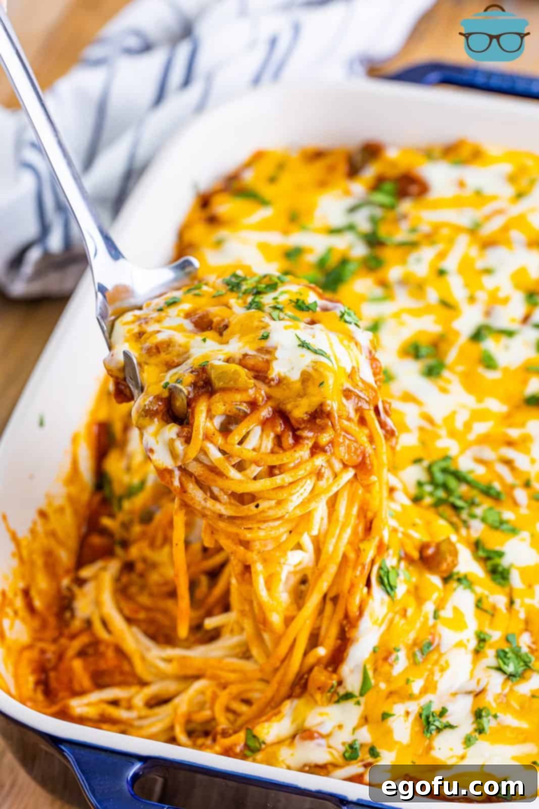 A baking dish full of Mexican million dollar spaghetti with a serving dish taking a serving out.