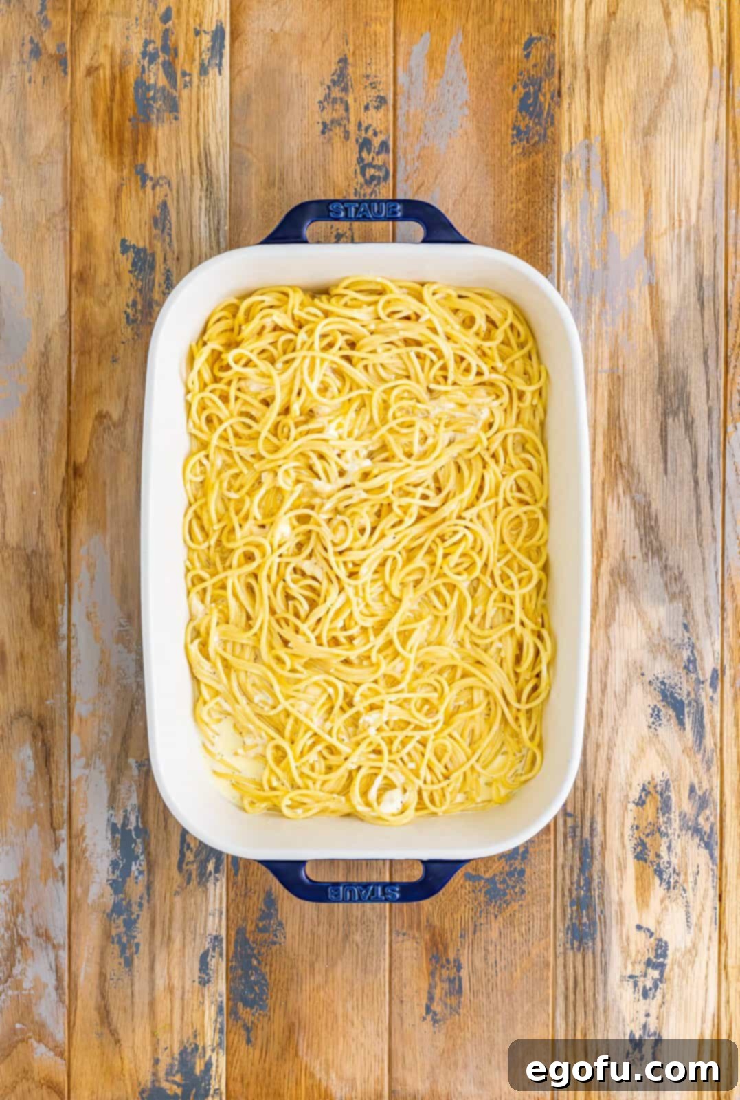 A baking dish with cooked spaghetti in a cream butter sauce.