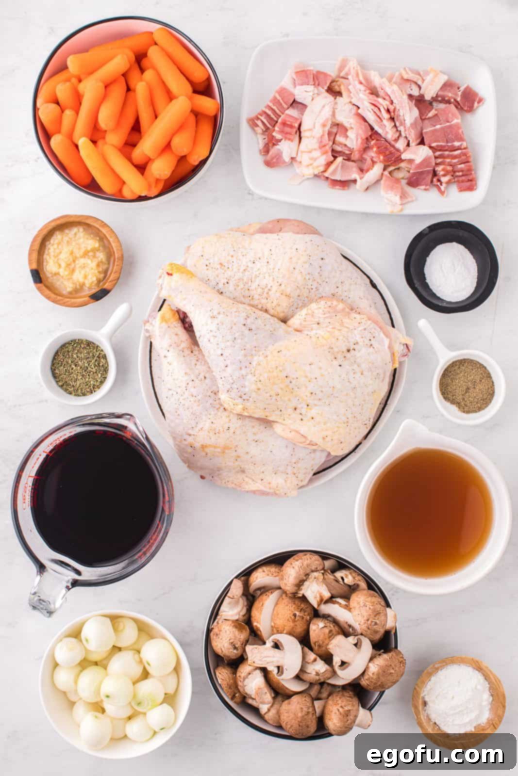 A flat lay of all the fresh ingredients needed for Coq Au Vin, including chicken quarters, bacon, various vegetables, and spices.