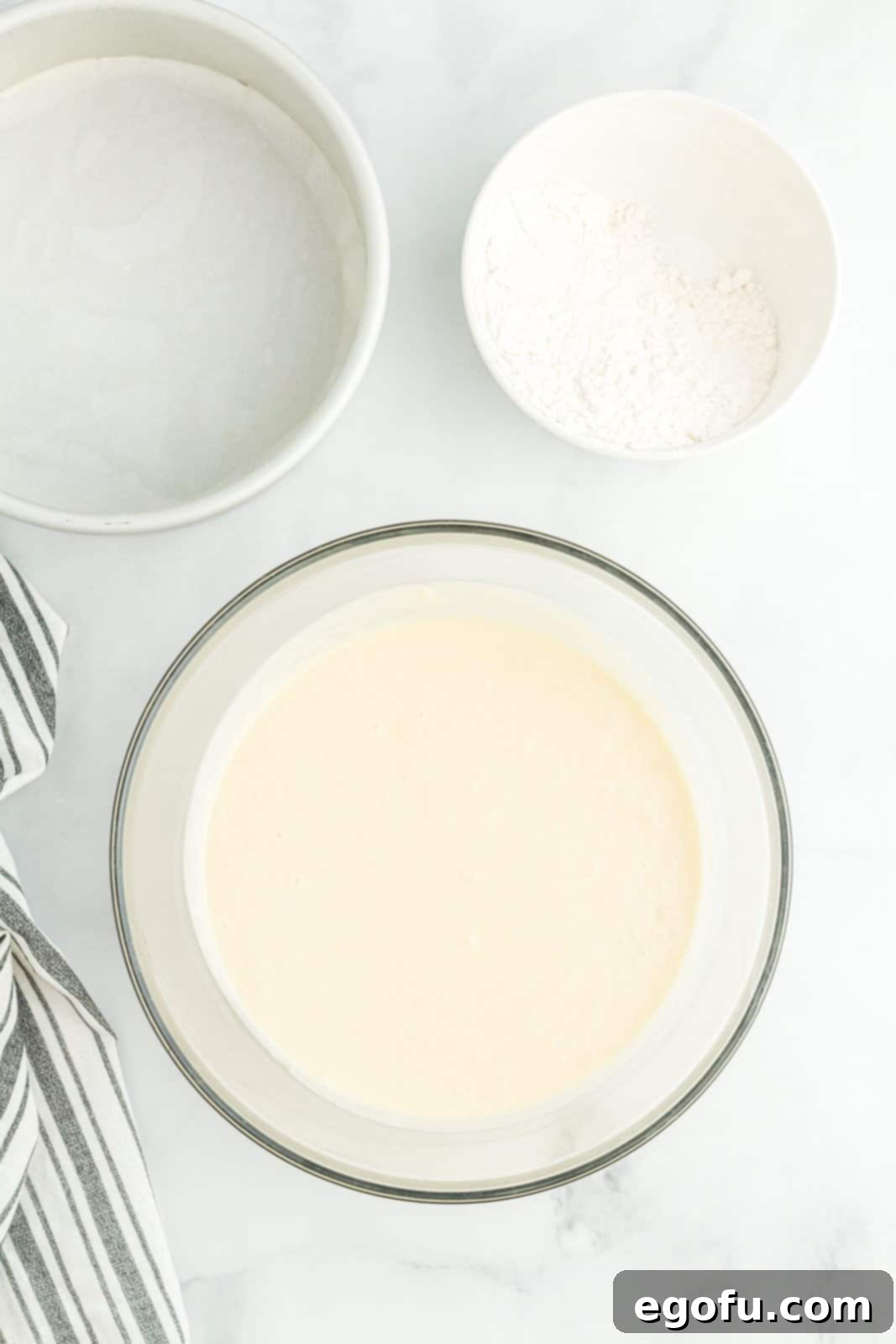 Dry ingredients and wet ingredients being mixed in a mixing bowl to create a homemade white cake. 
