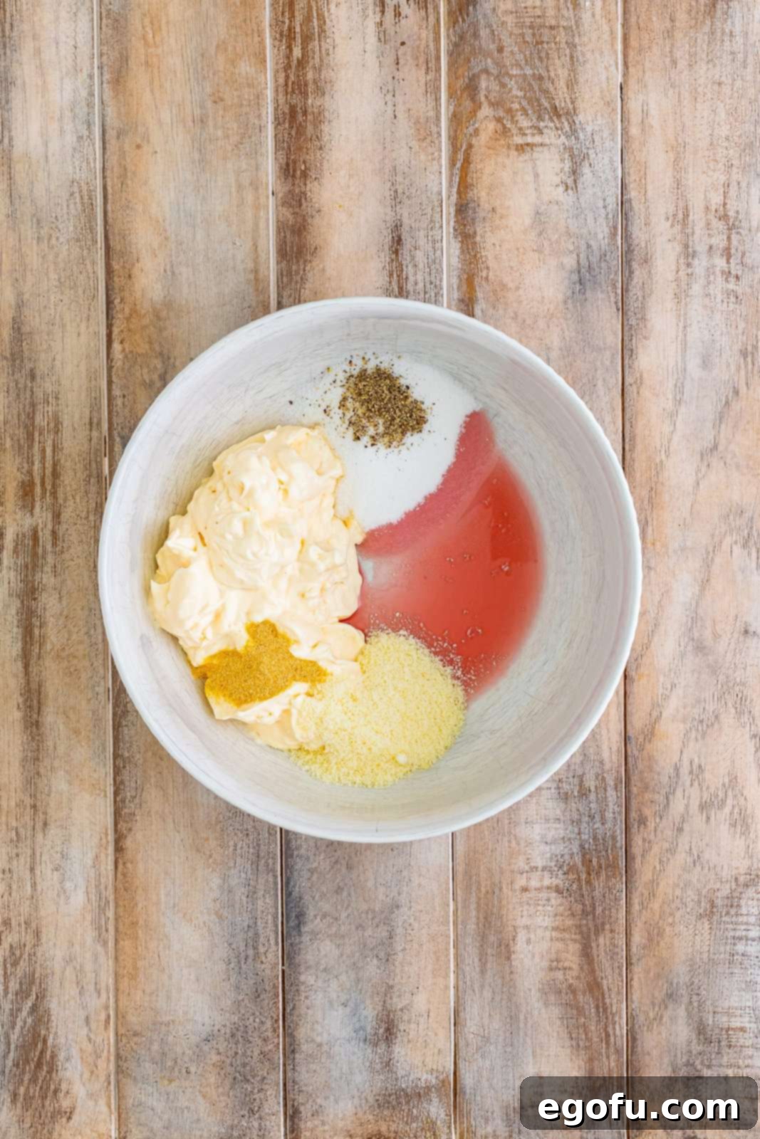 A mixing bowl with the creamy homemade dressing, consisting of mayonnaise, sugar, parmesan cheese, red wine vinegar, garlic powder, and black pepper, ready for the vegetables.
