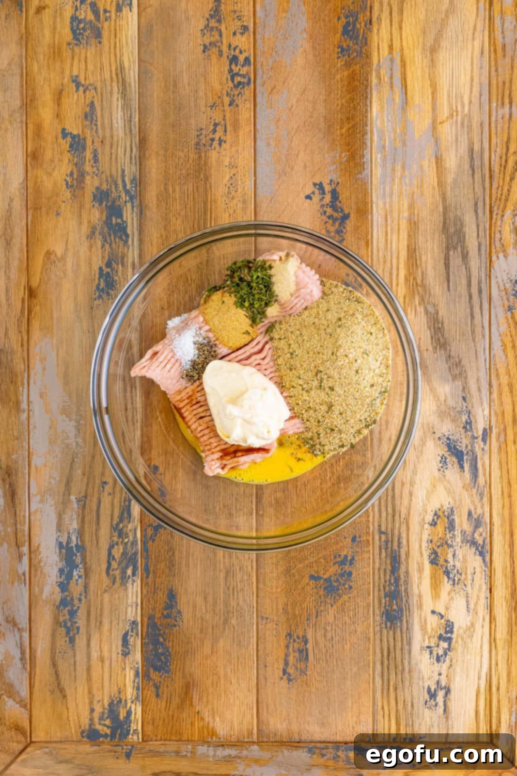 Mixing bowl with ground chicken, breadcrumbs, beaten egg, mayonnaise, Worcestershire sauce, garlic powder, parsley flakes, onion powder, pepper, and salt.