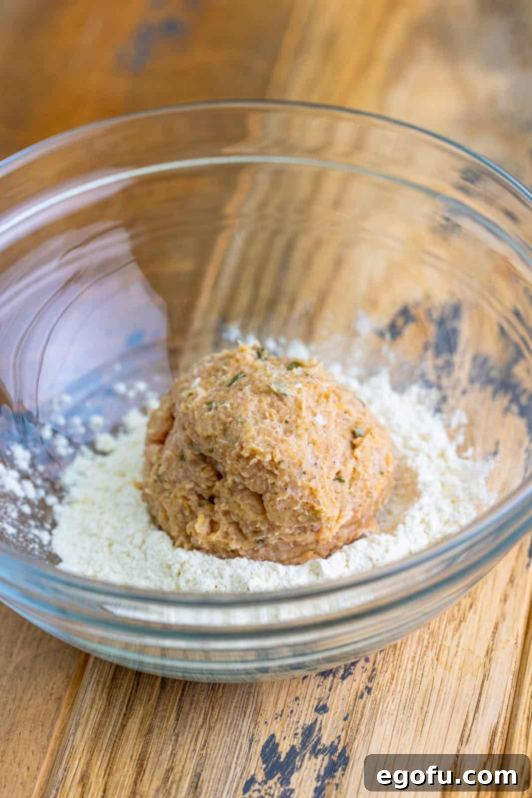 Ground chicken and spices in a ball in a bowl of flour.