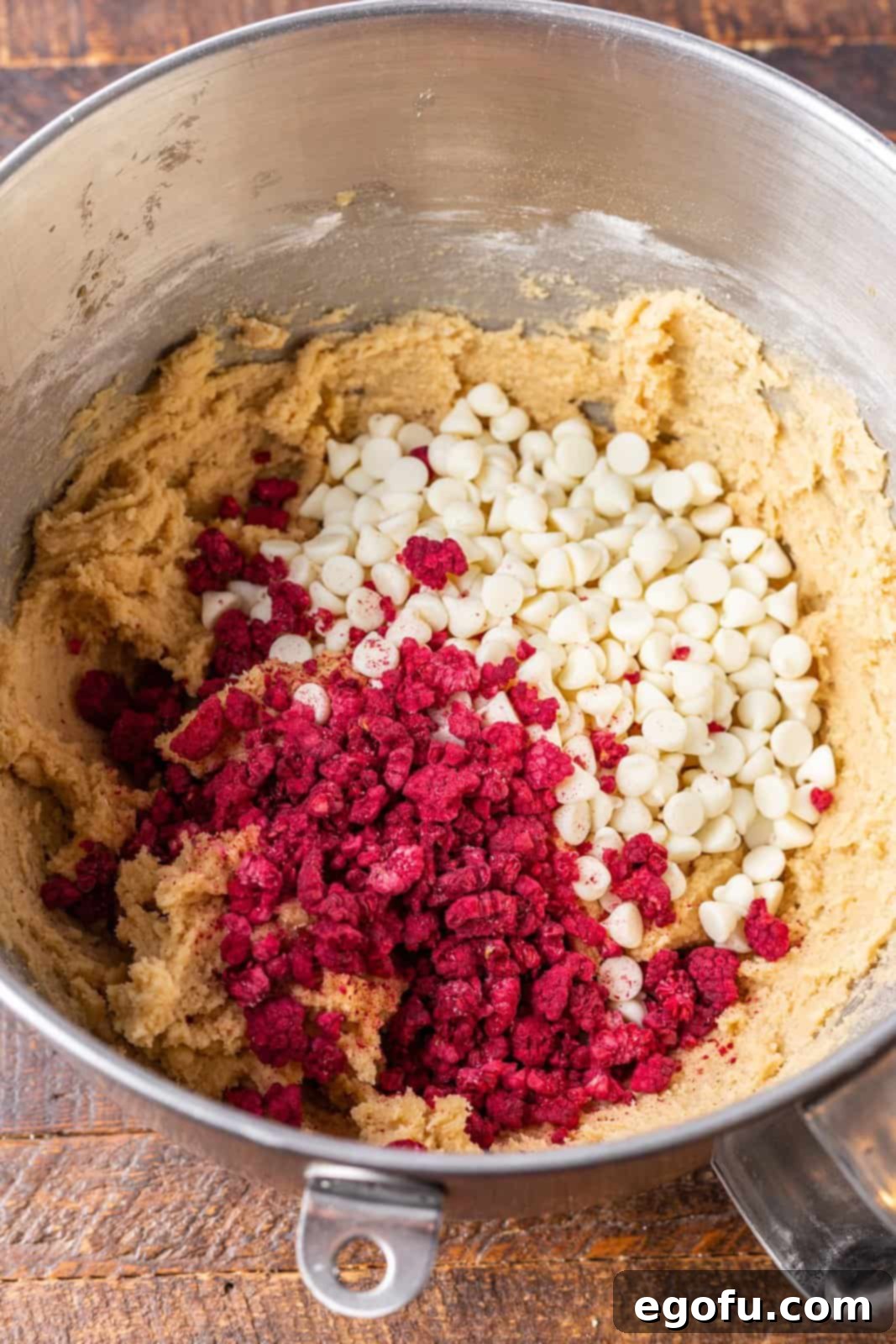 Subway Raspberry Cheesecake Bliss Bites 8 Beyaz çikolata parçacıkları ve dondurularak kurutulmuş ahududular, hazırlanan kurabiye hamuruna bir lastik spatula ile karıştırılıyor.