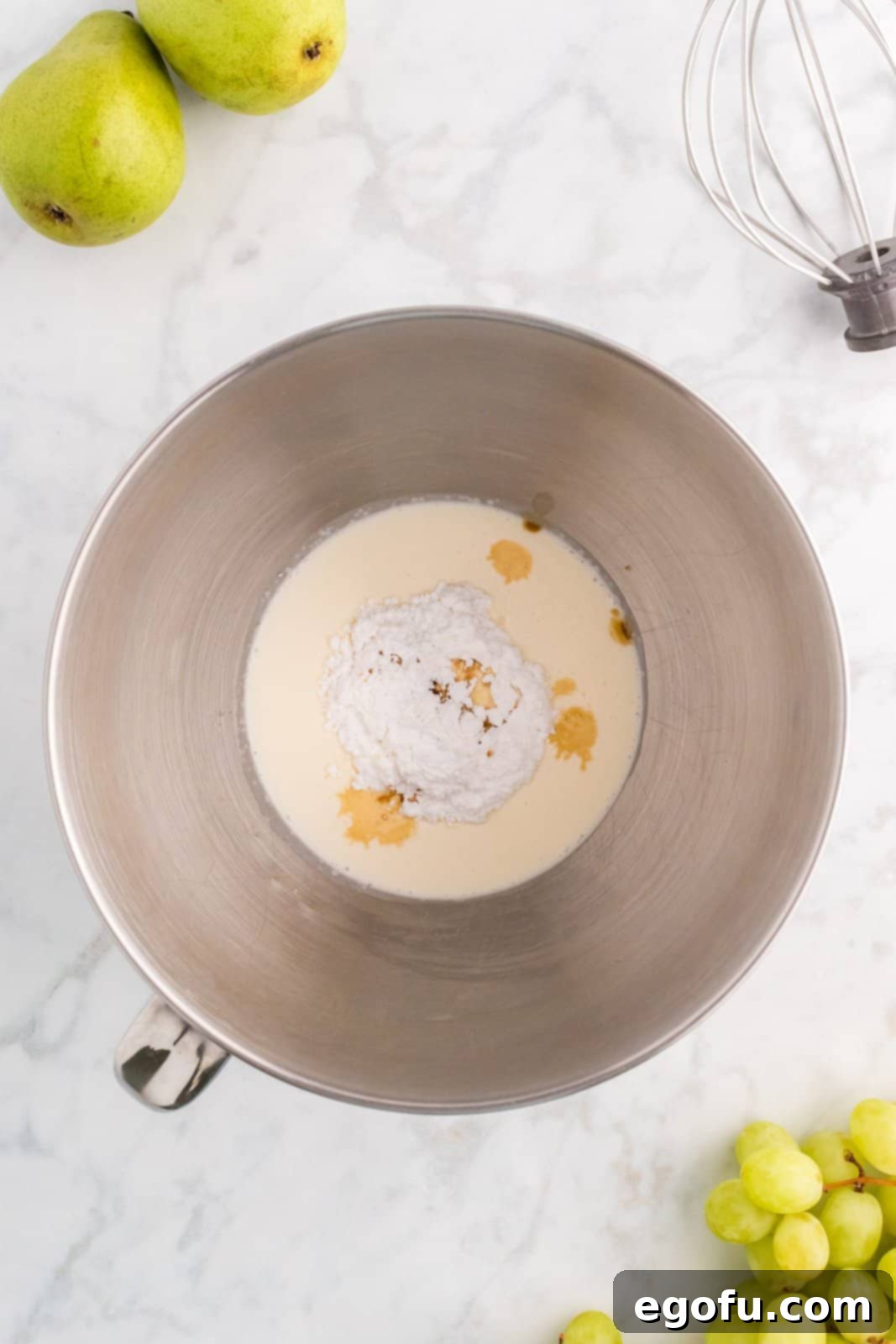 Emerald and Golden Ambrosia Delight 5 A mixing bowl filled with heavy whipped cream, vanilla extract, and powdered sugar, being prepared for whipping.