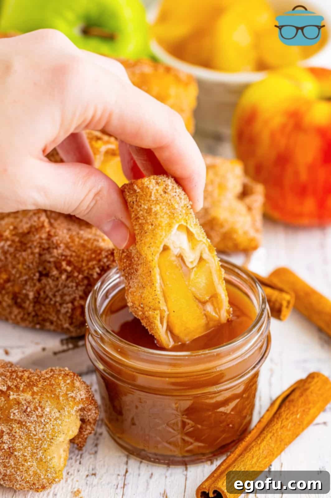 An apple pie egg roll being dipped in a sweet caramel sauce.