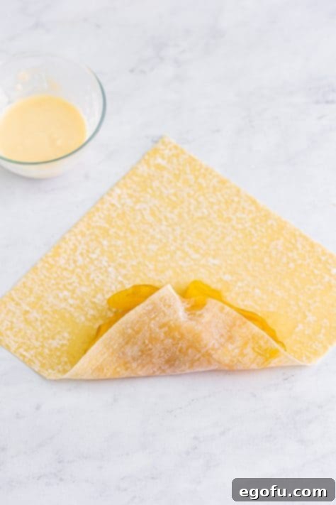 An egg roll wrapper with apple pie filling that is starting to be rolled up.