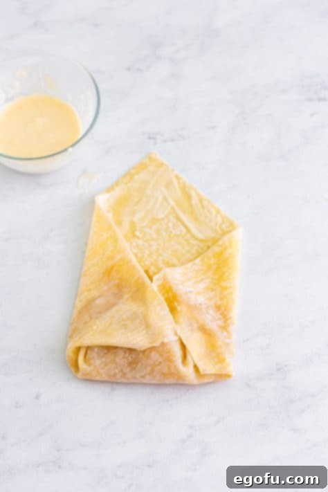 An egg roll wrapper being rolled up, filled with apple pie filling.