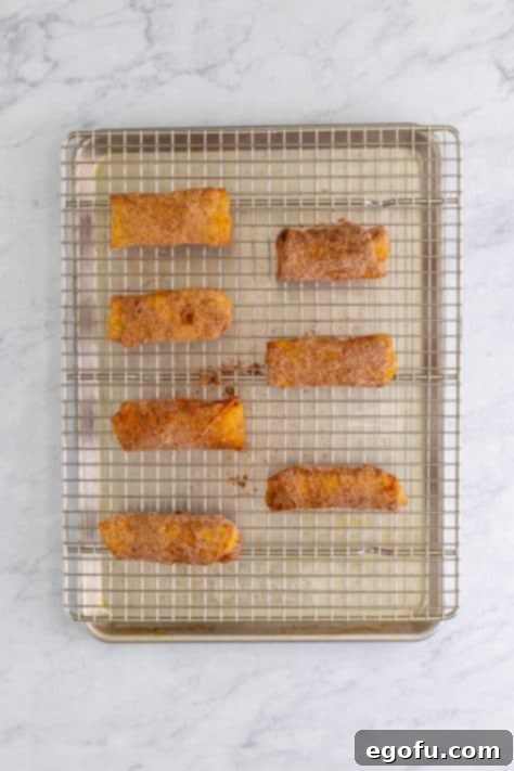 Cinnamon sugar coated apple pie egg rolls on a wire rack and baking sheet.