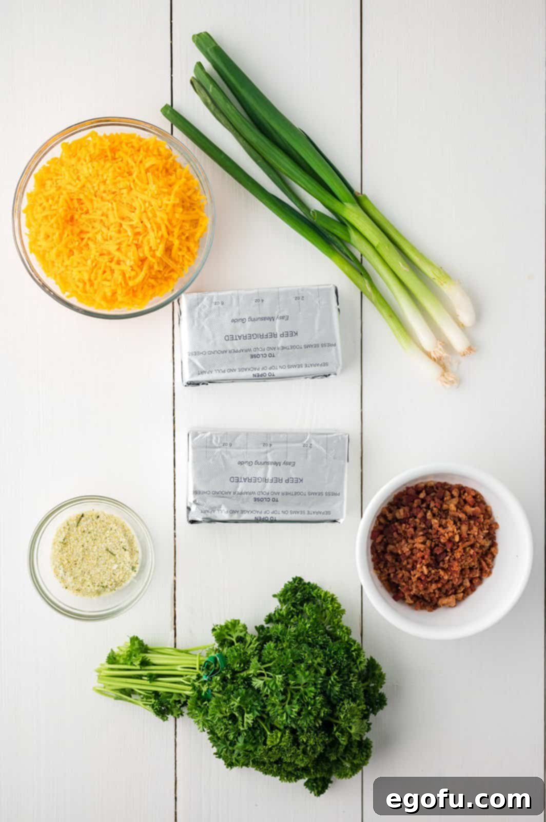 Bunny's Garden Cheeseball 4 A visual display of all the primary ingredients required for the Easter Carrot Cheeseball recipe, including softened cream cheese, crispy bacon bits, freshly sliced green onions, a packet of ranch dressing mix, shredded cheddar cheese, and a bunch of curly parsley.