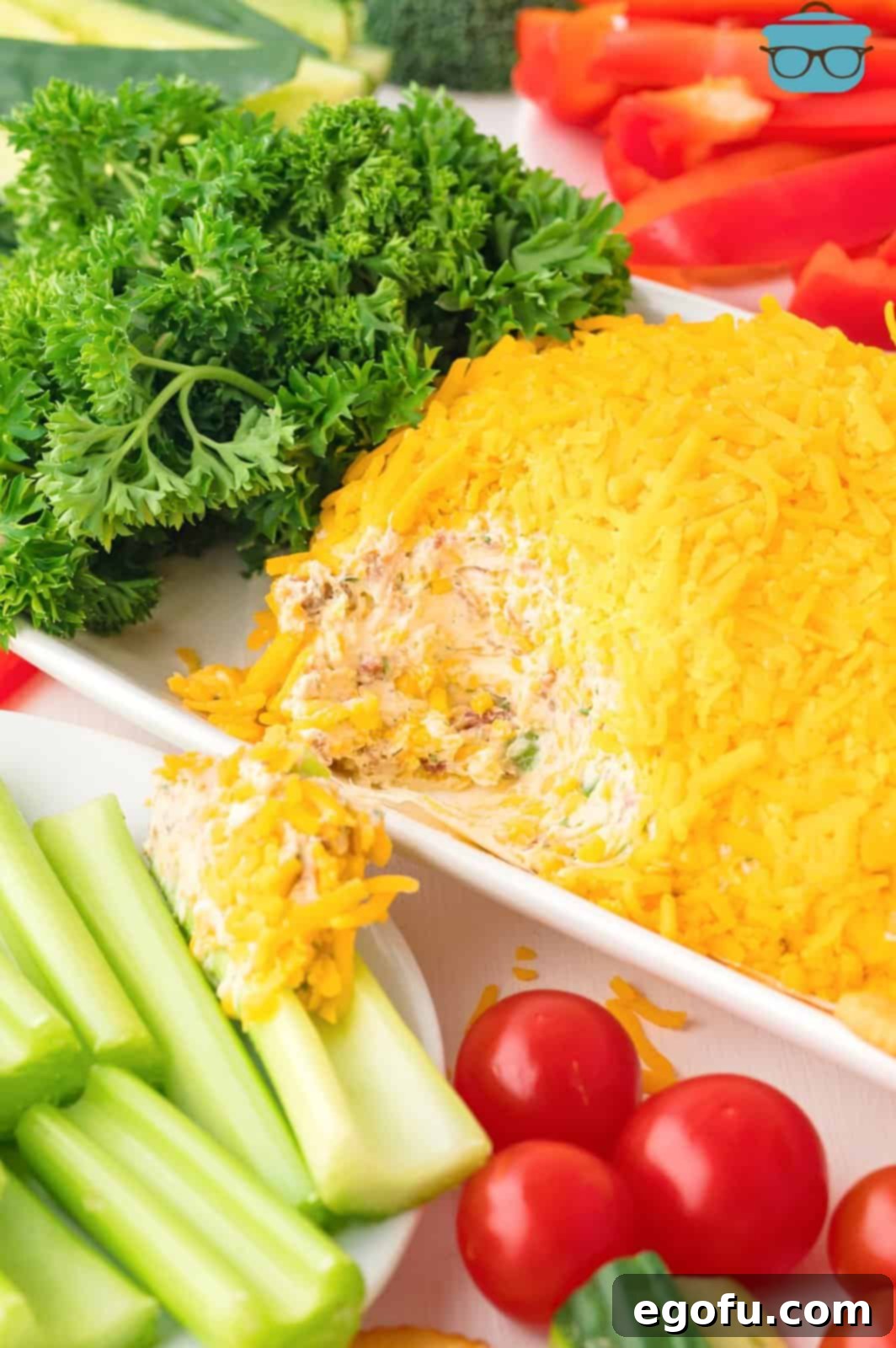 Bunny's Garden Cheeseball 9 A beautifully presented carrot cheeseball with its green parsley top, surrounded by fresh veggies, with a portion already scooped out, showcasing its creamy interior.