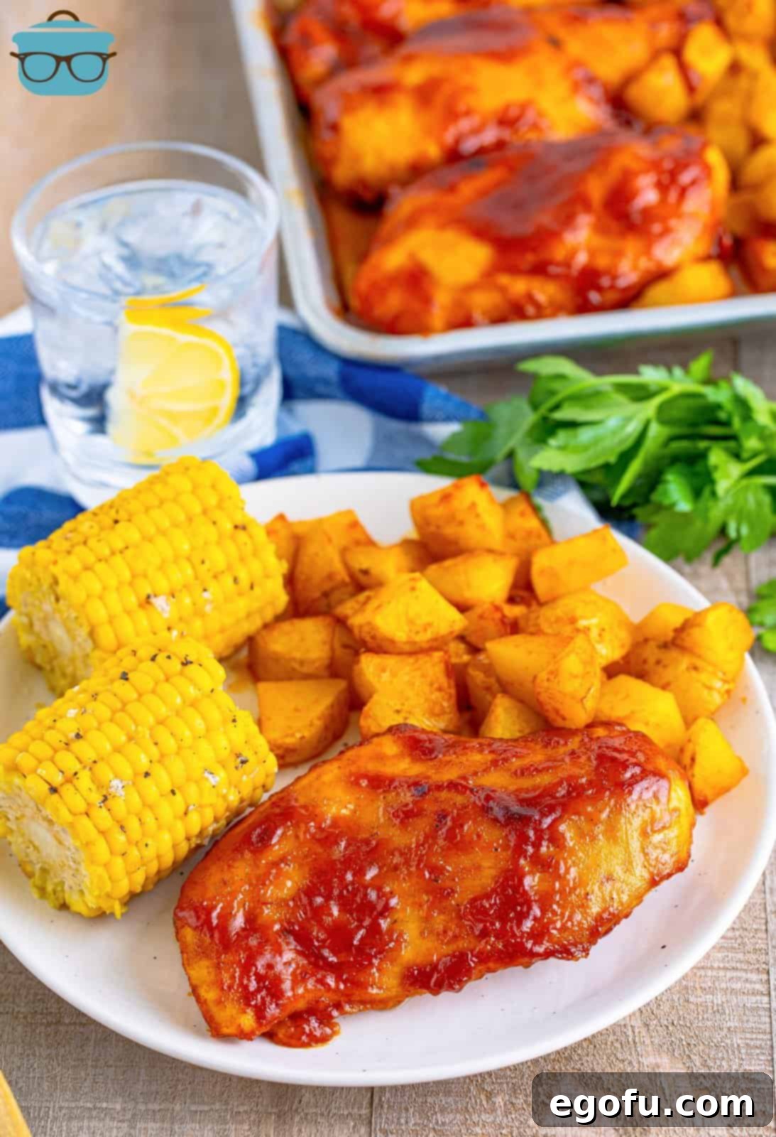 One-Pan BBQ Chicken Dinner 11 A plate of BBQ Chicken, crispy roasted potatoes, and sweet corn next to the sheet pan it was cooked on, ready to be enjoyed.