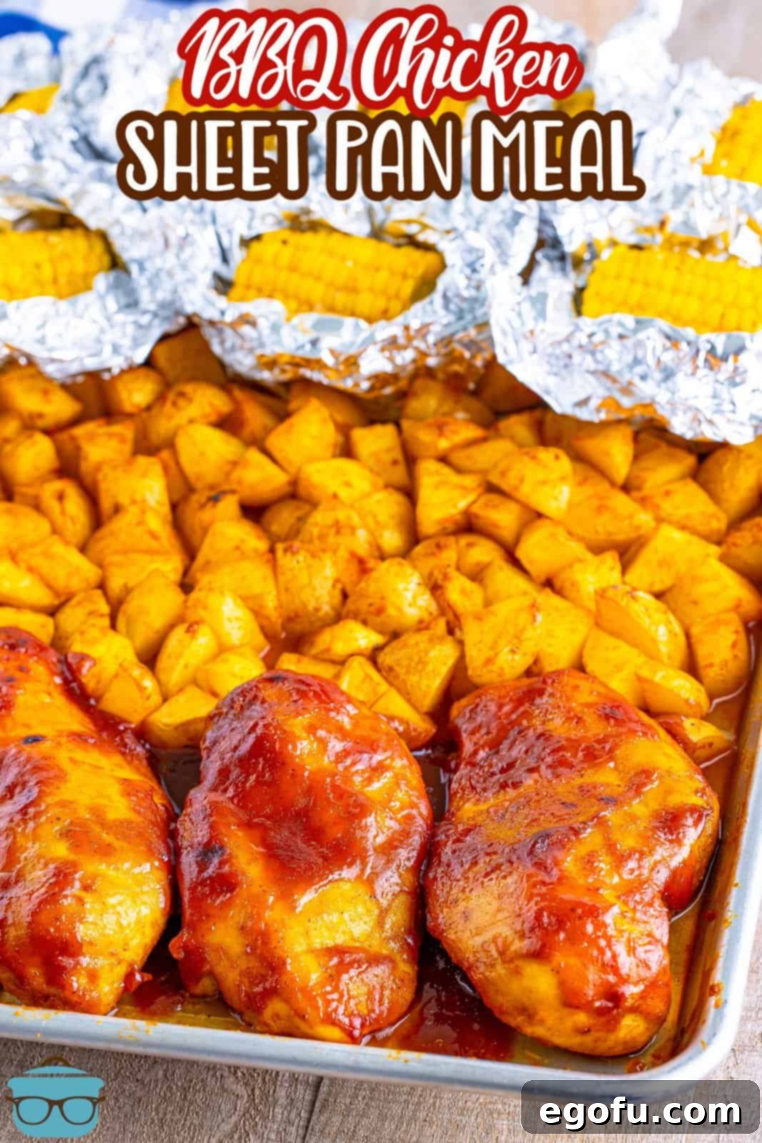 One-Pan BBQ Chicken Dinner 3 Corn on the cob wrapped in aluminum foil, a section of roasted potatoes, and some BBQ chicken pieces on a sheet pan.