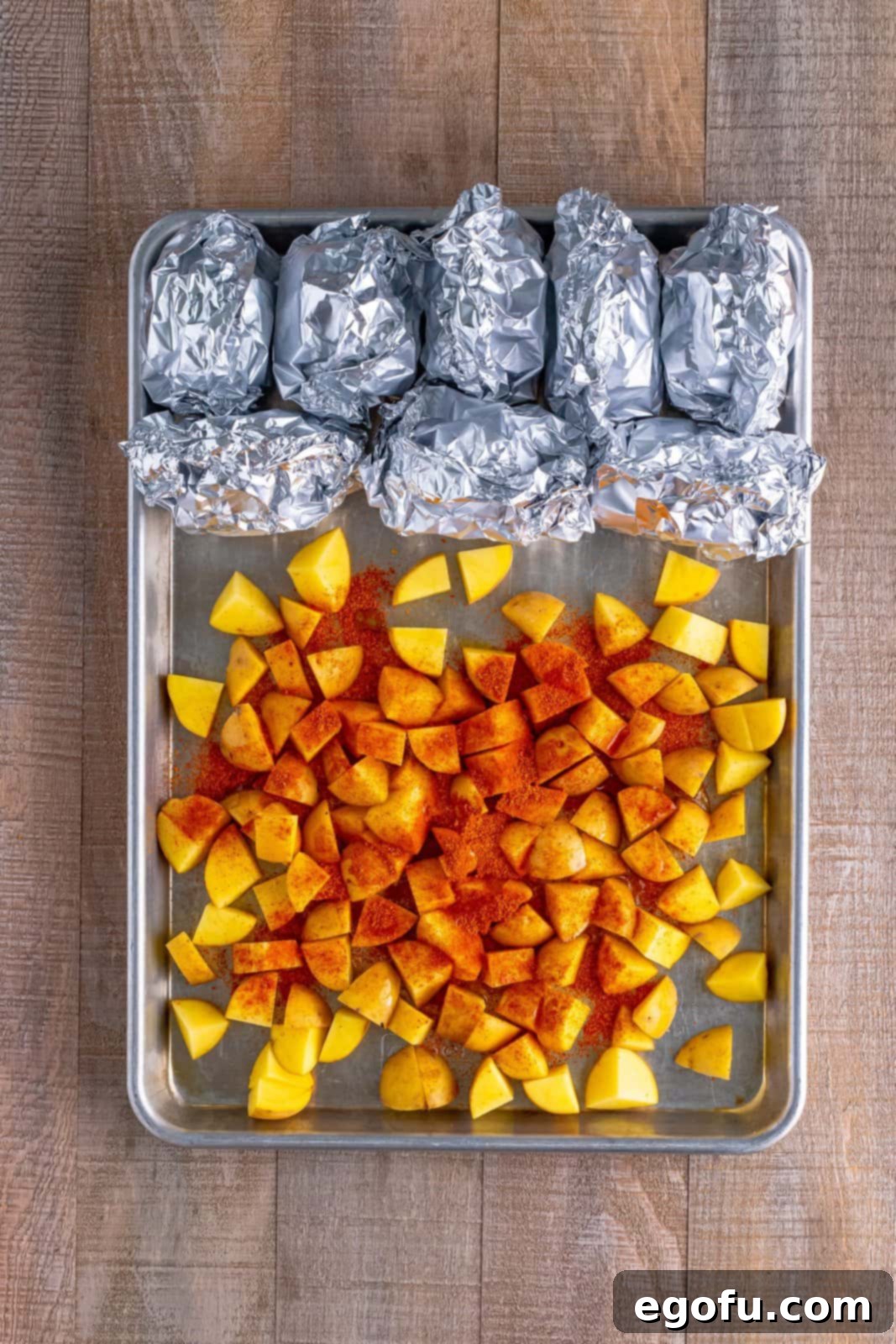 One-Pan BBQ Chicken Dinner 6 A sheet pan with rolled-up mini corn on the cobs at one end and diced potatoes with seasoning in the center.