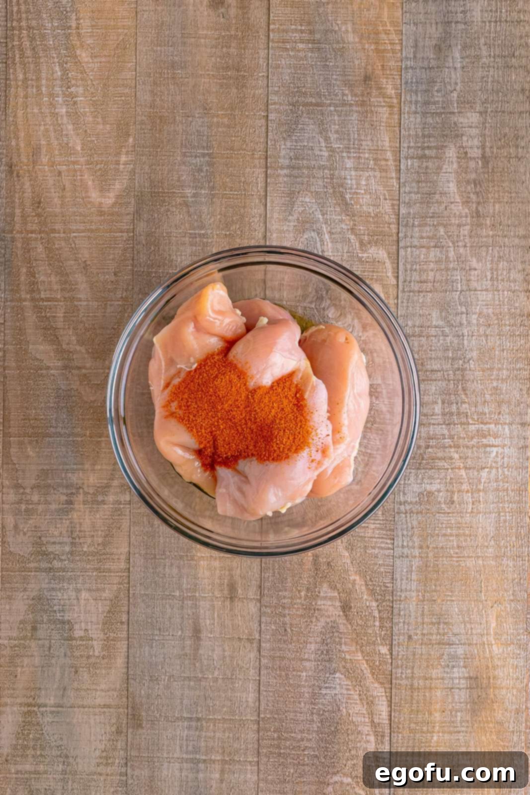 One-Pan BBQ Chicken Dinner 7 A glass mixing bowl containing chicken breasts coated in BBQ seasoning and olive oil.