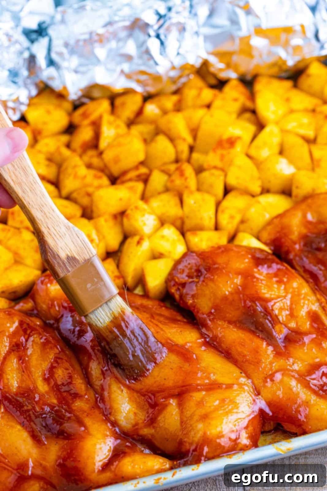 One-Pan BBQ Chicken Dinner 9 A basting brush applying BBQ sauce onto a chicken breast on a sheet pan.