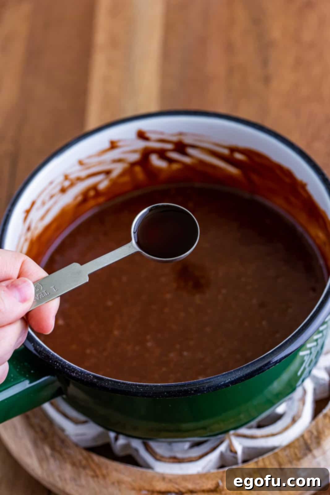 Vanilla extract being stirred into the finished chocolate frosting mixture.