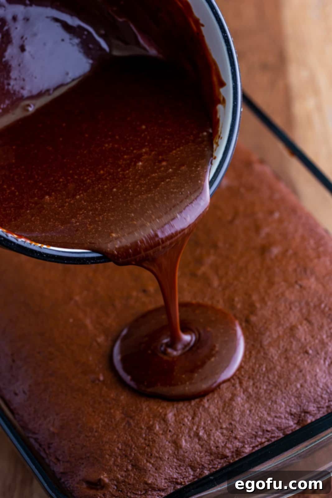 Rich chocolate frosting being poured and spread over the cooled Dr Pepper Cake.