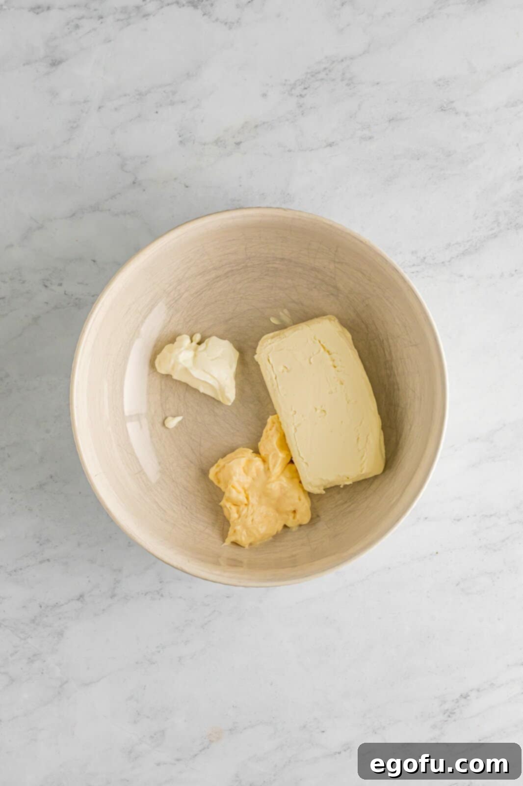 A medium-sized mixing bowl containing a creamy, smooth mixture of softened cream cheese, rich mayonnaise, and tangy sour cream, ready for the next ingredients to be added.