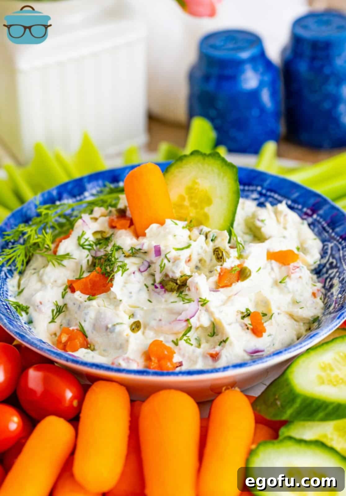 A rustic wooden board showcasing a generous bowl of creamy smoked salmon dip, surrounded by an abundant assortment of vibrant, crunchy vegetables like cucumber, carrots, celery, and bell peppers, perfect for a healthy and delicious appetizer spread.