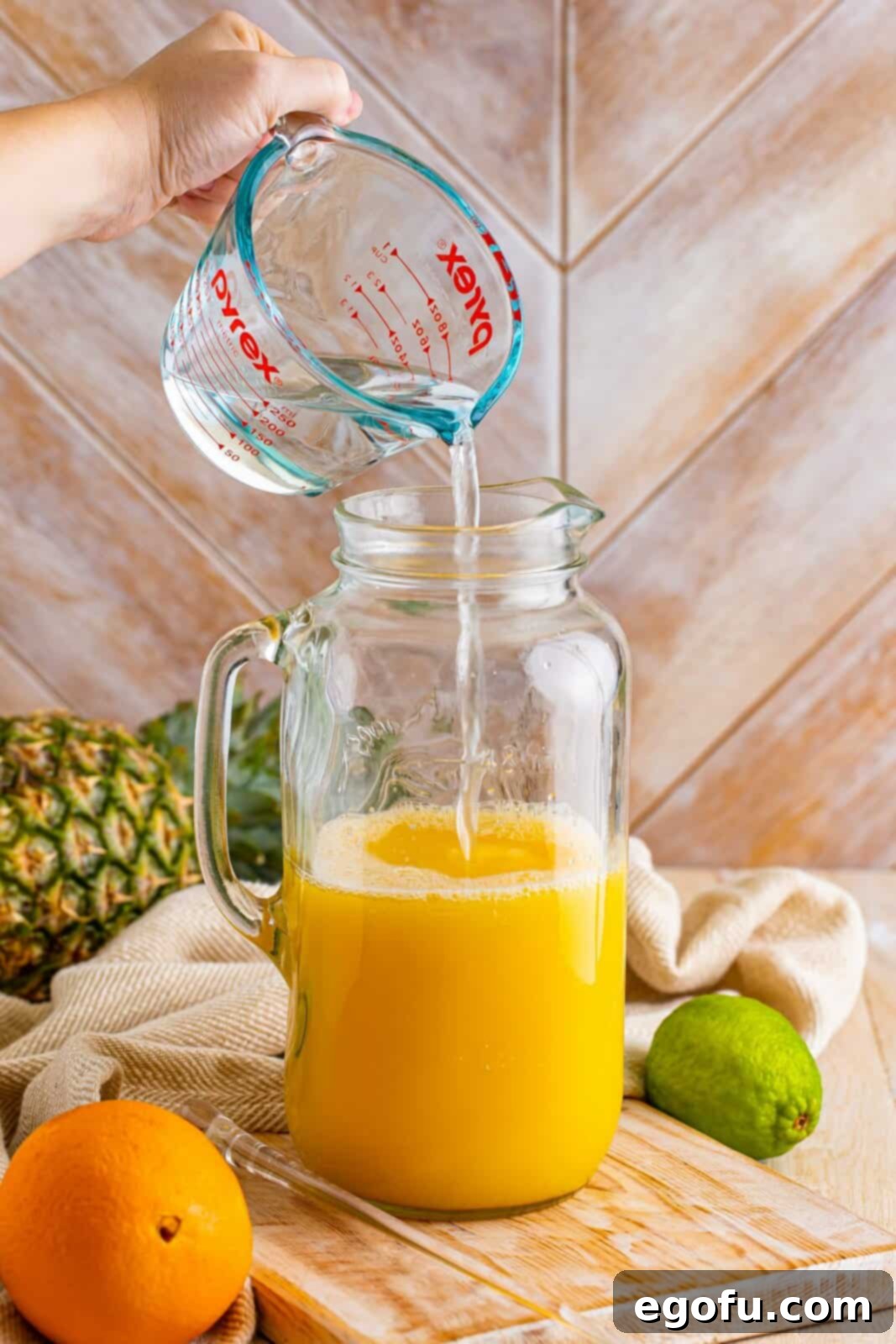 Island Dream Sip 5 A pitcher with pineapple, orange juice, and white rum being mixed for Rum Punch.