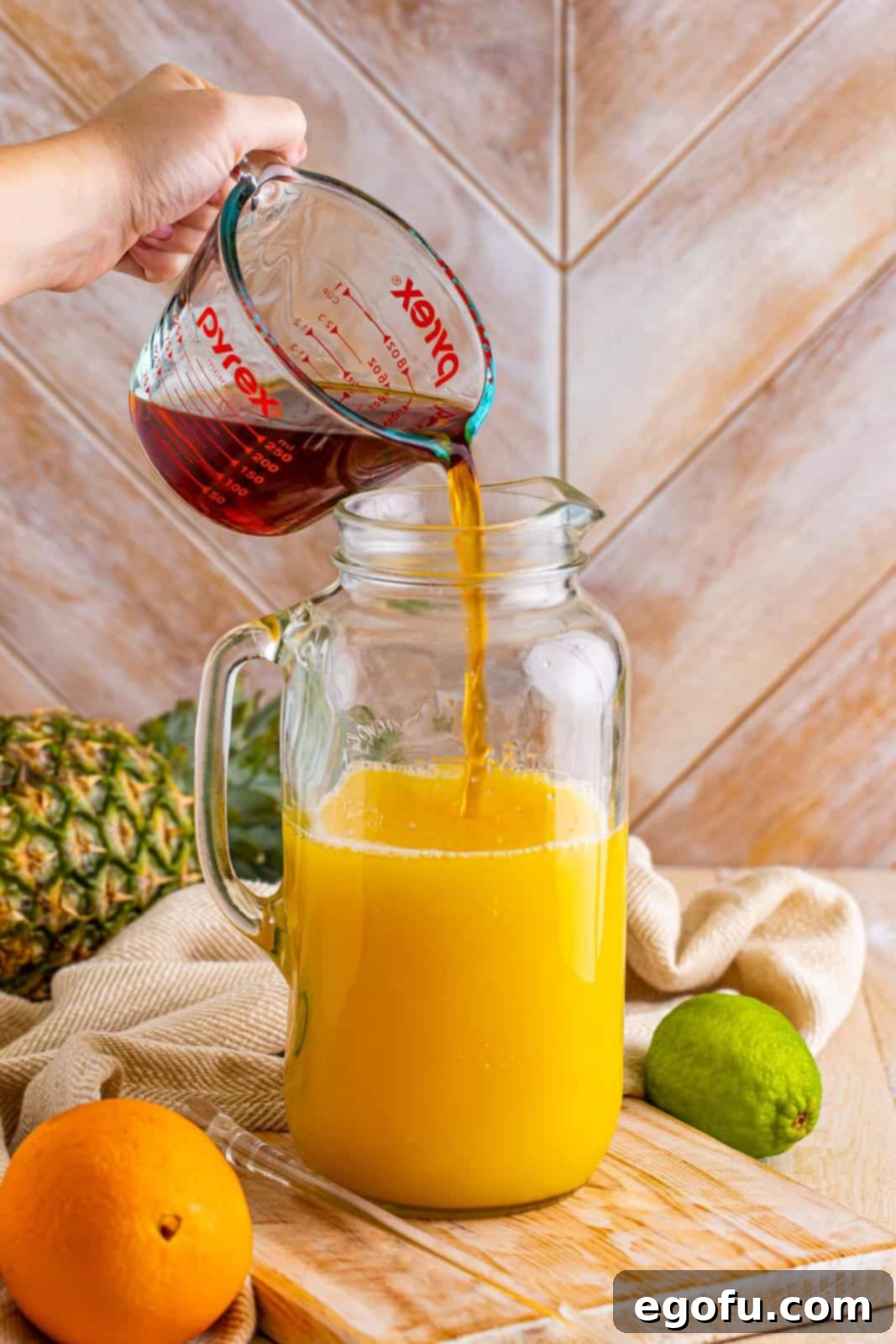 Island Dream Sip 6 A pitcher with pineapple, orange juice, dark rum, and white rum, plus lime juice being added.