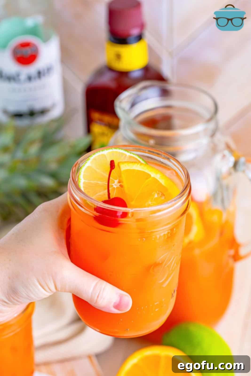 Island Dream Sip 9 A hand holding a glass of Rum Punch, garnished with an orange slice and cherry.