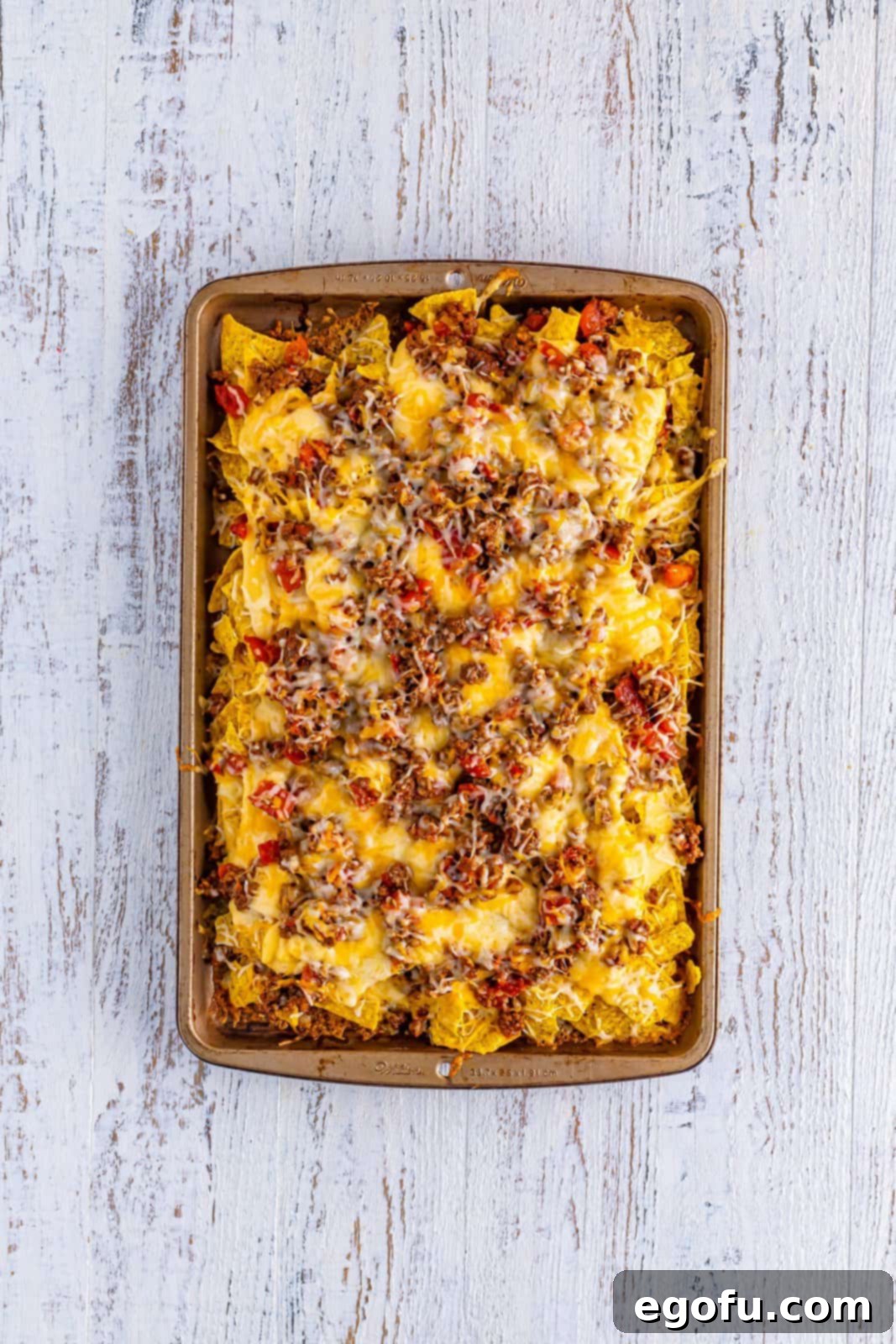 Baked, layered sheet pan nachos fresh out of the oven, with perfectly melted cheese and warmed toppings.